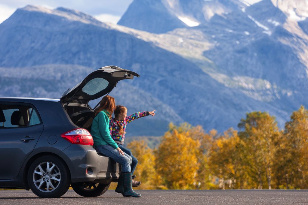 Mum and child sitting in the boot of their car looking over a natural, mountain range and forest